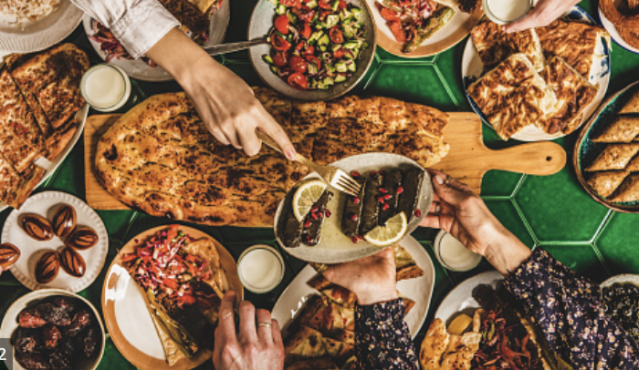 Food on a large table, pizza in the centre. People hands reaching for food