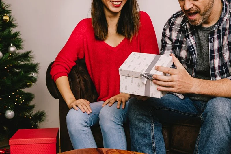 A man opens a wrapped gift, showcasing the best Christmas presents for men.