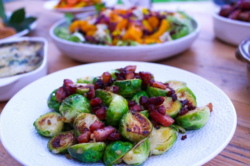 A plate of crispy Brussels sprouts with bacon, a cheap, easy New Year's Eve food.