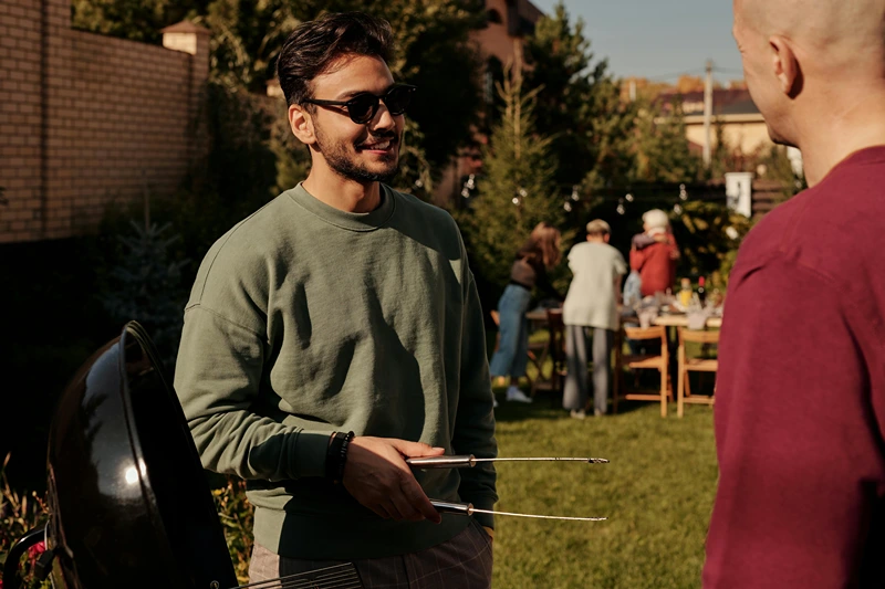 Two men grilling BBQ and conversing, showcasing summer dinner party ideas.