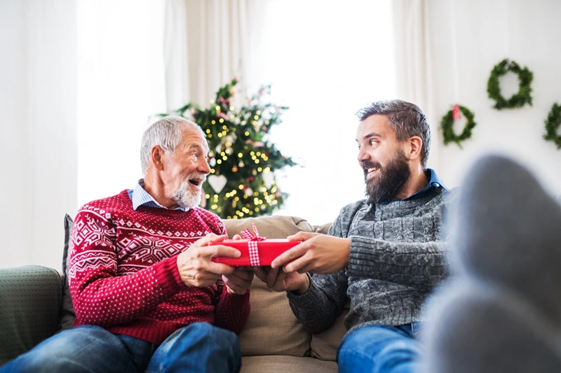 An old man happily accepts presents, showcasing unusual Christmas gifts for him.