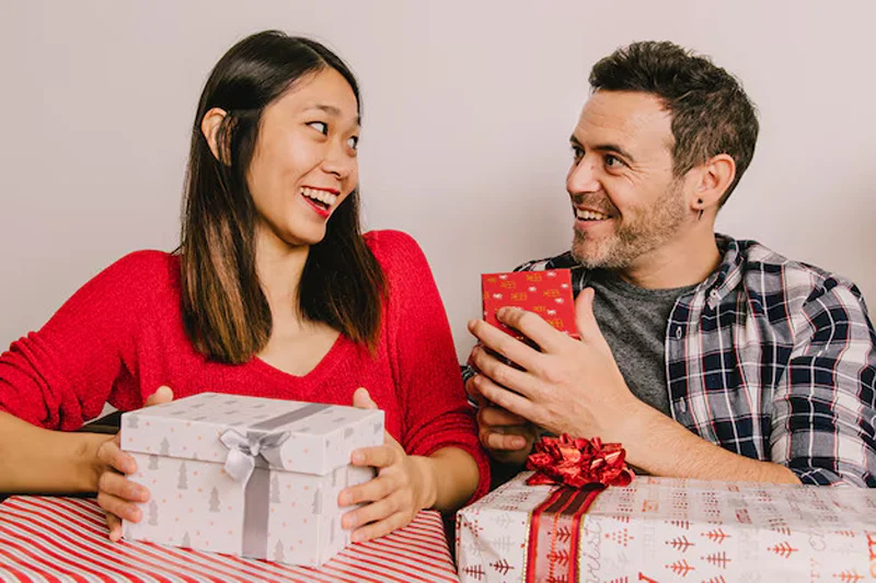 A man holding a gift out to a woman, answering what to get girlfriend for Christmas.
