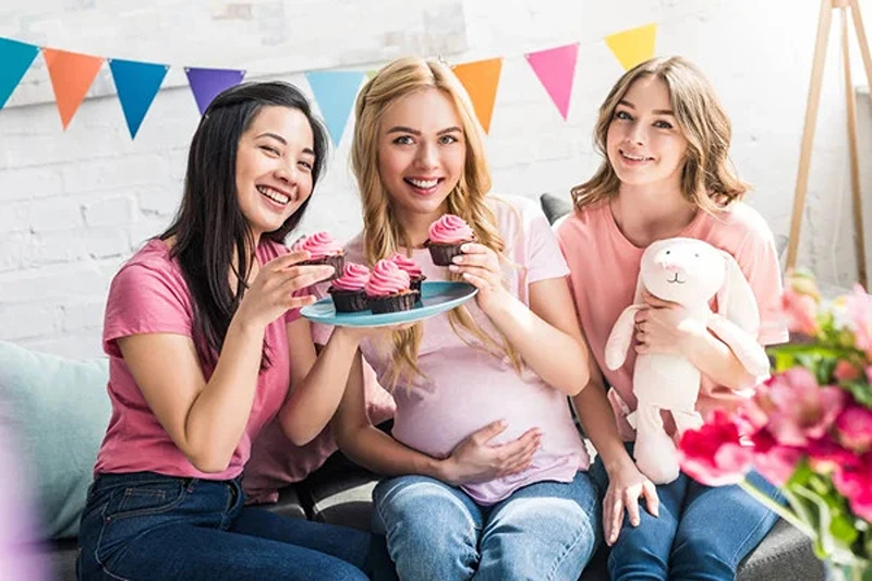 Expectant mother and friends enjoying cupcakes from baby shower food catering.